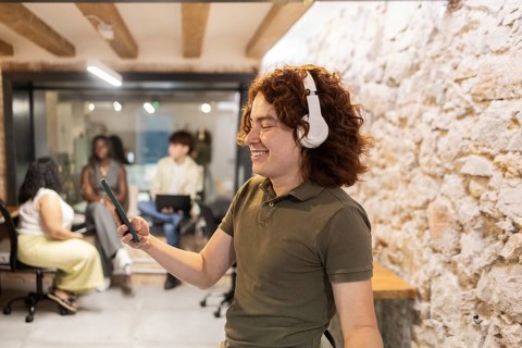 Side view of a young man with headphones and a smartphone enjoys working in a lively summer