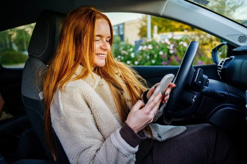 A beautiful pregnant girl with vibrant red hair sits in a car, smiling as she engages with her
