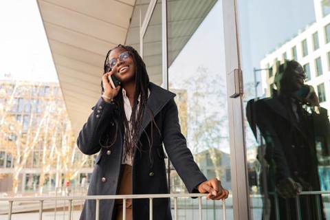 A cheerful young African American businesswoman with braids talks on her mobile phone during a