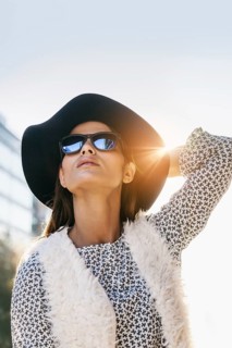 Woman wearing a floppy hat, sunglasses, and textured vest. Her confident pose and bright sunlight