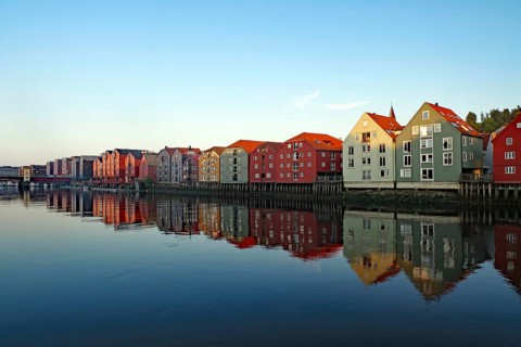 Row of colorful houses along a quiet river with reflections in the water, Nidelva, Trondheim,