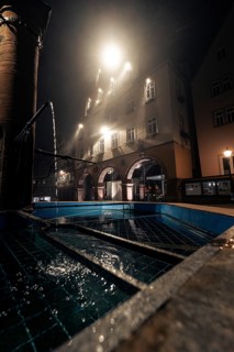Night scene with illuminated building and fountain in the foreground, creating a mysterious