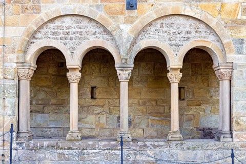 Three Romanesque arches with columns on a rustic stone wall, showing medieval architectural