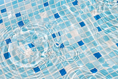 A close-up image of mosaic tiles under clear, rippling water, creating a serene and refreshing