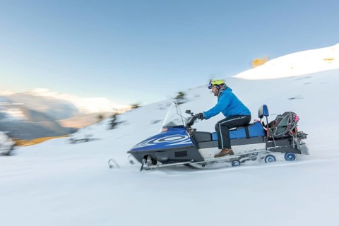 A snowmobile rider in a blue jacket speeds through a snowy landscape, showcasing the thrill of