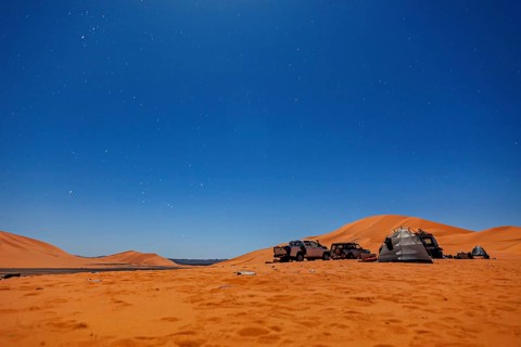 Camp in the desert under a starry night sky with tents and vehicles, tent camp in the dunes of the