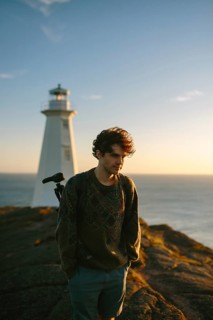 A young man stands by the Cape Spear Lighthouse in Newfoundland & Labrador, Canada, enjoying a