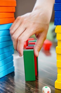 A close-up of a hand carefully removing a green wooden block in a colorful stacking game. The scene