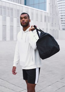 A confident black male athlete stands in an urban setting, wearing a white hoodie and shorts. He