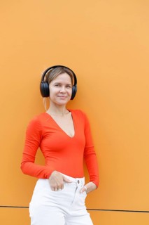 A woman in an orange top stands confidently against a vibrant orange wall in Warsaw, sporting