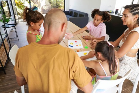 A family enjoys a creative activity together at home, seated around a table. The joyful moment
