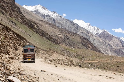 A colorful truck traverses a rugged dirt road in the stark, mountainous landscape of Zanskar
