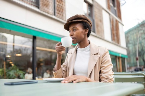 A stylish black woman sips coffee at an outdoor cafe, embodying urban elegance and relaxation The
