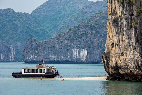 A ship in a calm bay with a rocky landscape and floating people, tourists on a tour boat in Halong