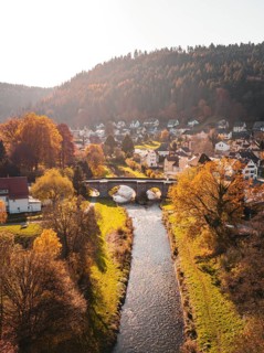 Autumn scene of a village with bridge and river amidst trees and wooded hills, Calw, Black Forest,