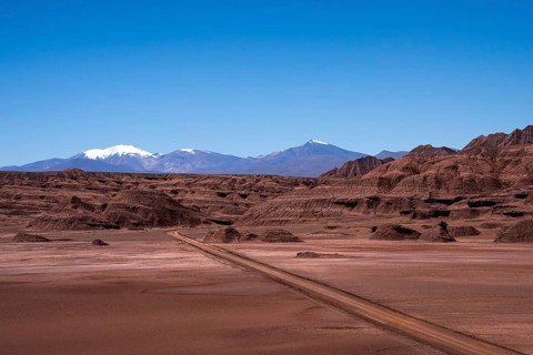 A scenic view of a winding dirt road cutting through the barren, textured terrain of La Puna in