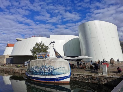 Ozeaneum in Stralsund, modern building with curved shapes next to a water channel under cloudy sky,