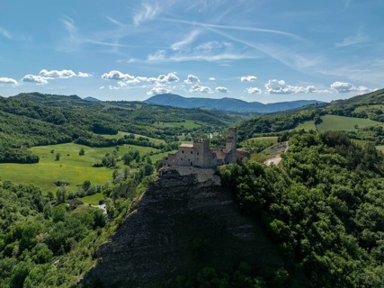 Drone view of a historic stone castle perched on a rocky hill surrounded by green rolling hills and