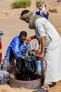 Two men in traditional dress work together to collect water in an arid landscape, Tuareg draw water
