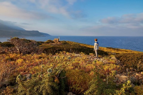 A boy stands on a coast and looks at the sea under a blue sky, morning light, Tsichli Babas islet,