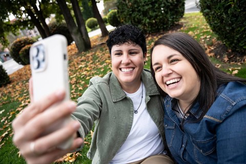 A joyful curvy lesbian couple takes a selfie in a park surrounded by autumn leaves. Their happiness