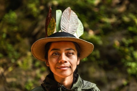 Close-up portrait of a young Ecuadorian woman adorned with leaves in her hat, set against the green