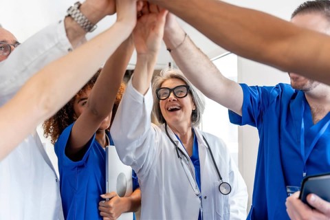 Happy mature female doctor high fiving with a diverse healthcare team, symbolizing unity, success,