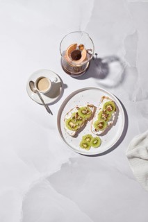 Delicious kiwi toast topped with creamy cheese, crunchy walnuts, and chia seeds on a white plate. A