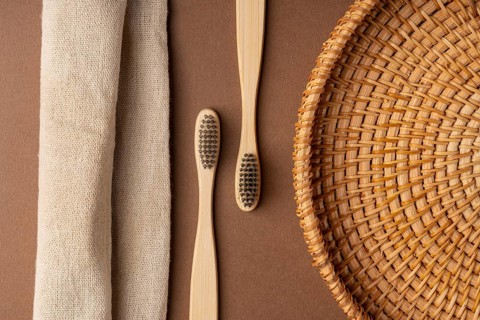 Top view of bamboo toothbrushes on a brown background, accompanied by a woven basket and a linen