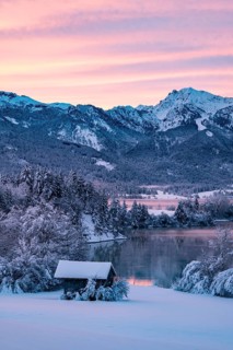 Dawn and sunrise at the wintry Forggensee in a snow-covered winter landscape in the foothills of