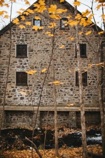 A historic stone building nestled among vibrant autumn foliage in Quebec, Canada. The rustic