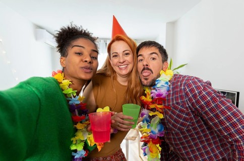 Three friends enjoying a lively birthday celebration at home. They wear colorful leis and festive