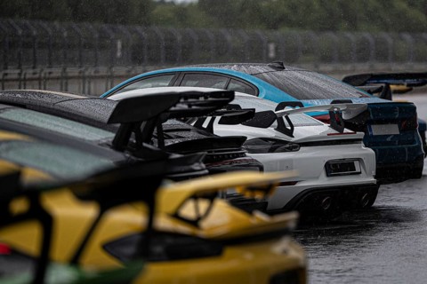 A stunning lineup of various sports cars, drenched by rain, parked on a race track, showcasing an