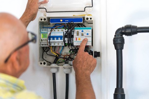 Back view of cropped unrecognizable senior male electrician examines and adjusts a circuit breaker