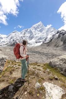 A woman trekker with a backpack and trekking poles takes in the breathtaking view of the snowy