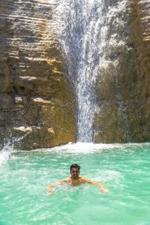 Happy male tourist swimming and enjoying the fresh water of a beautiful waterfall cascading down