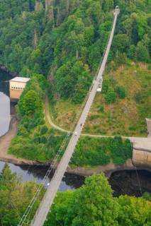 Aerial view of a bridge over a river, surrounded by lush forest and a steep slope,