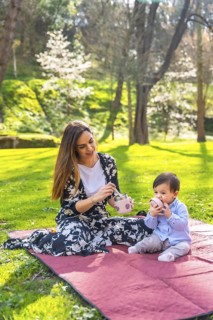 Young mother preparing a healthy snack for her baby while enjoying a sunny picnic on a blanket in a