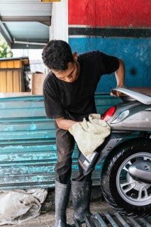 A motorcycle cleaner is meticulously polishing a bike's rear at a workshop. The scene captures