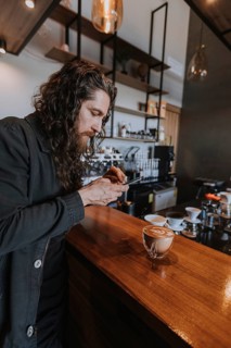 A man photographs his latte art in a modern cafe, highlighting coffee culture and social media