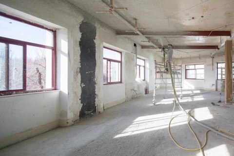 A spacious, well lit room under renovation, featuring scaffolding and a worker in protective gear