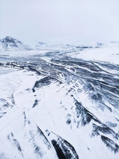 Aerial view of a vast Icelandic winter landscape blanketed in snow, showcasing intricate river