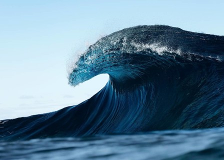 A stunning photograph captures the beauty of a large ocean wave cresting in the open sea against a