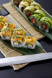 Variety of sushi rolls elegantly placed on a bamboo mat, with avocado and seafood toppings,