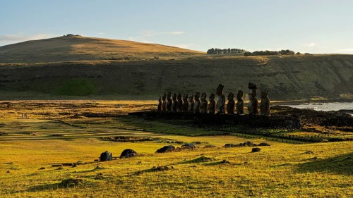 Ahu Tongariki with row of 15 moai statues on stone platform in morning light, grass hill and coast