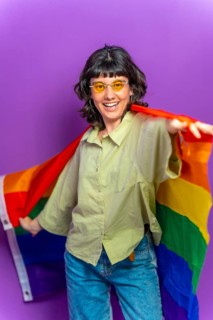 Studio portrait with purple background of a non binary latin woman dancing wrapped with lgbt
