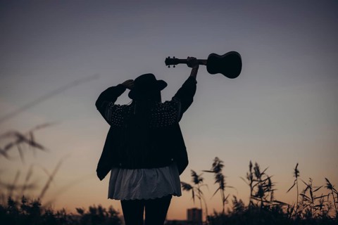 A silhouette of a woman raising her ukulele against a stunning sunset backdrop, capturing a moment