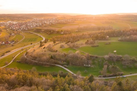 Aerial view of a rural landscape with fields, trees, a village and roads at dusk, e-bike tour, old