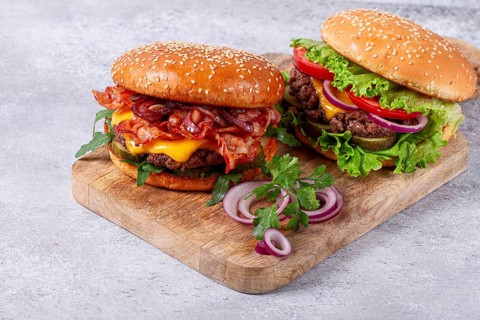 Two burgers with beef patty, fried bacon, cheddar cheese, tomatoes, homemade, no people