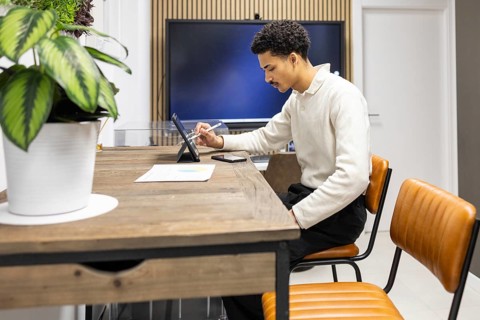 A professional working on a digital tablet in a modern office setting. The workspace features a